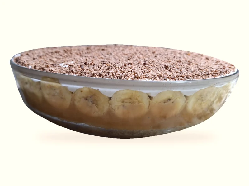 Banoffee em travessa transparente com rodelas de banana, camadas cremosas e raspas sobre a cobertura
